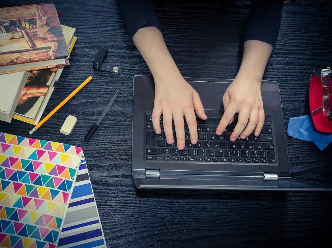 Photo of hands typing on computer surrounded by books
